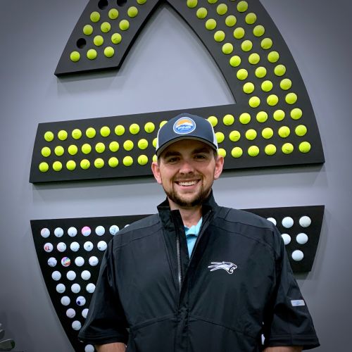 “Wyatt Larkin stands before Apex Golf logo, smiling, black jacket, golf balls backdrop.” 