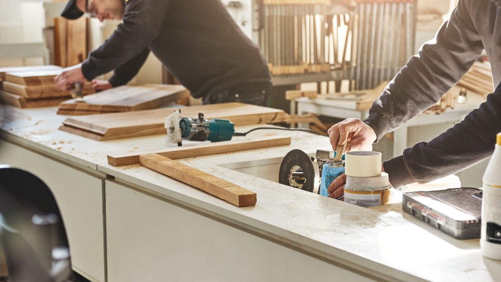 Two men working on a wood project at a bench in 7th Planet Woodshop, rustic setting.