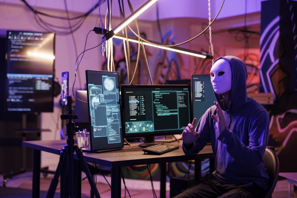 “Person in black hoodie, white mask, war room with computers, red haze, 7th Planet Contact.”